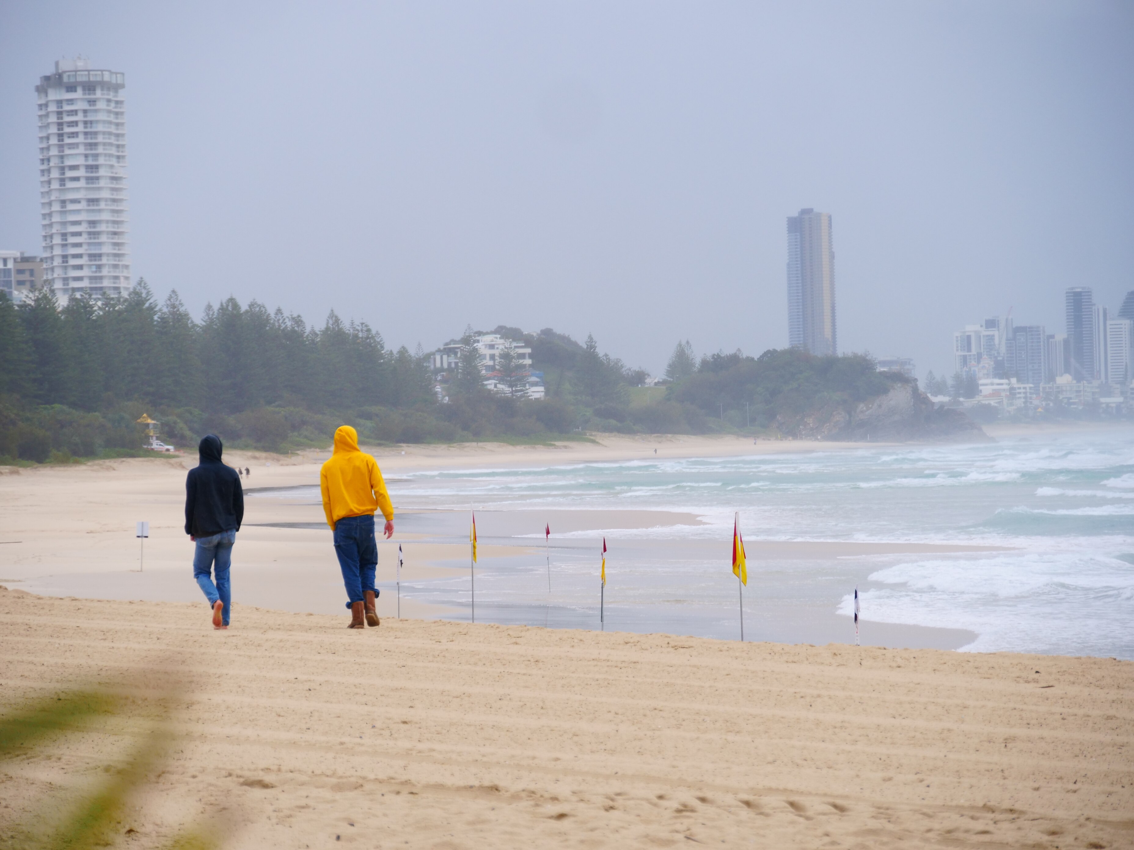 Two people in raincoats walking on a gloomy beach with flags