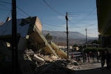 People walk next to a destroyed house after an earthquake.