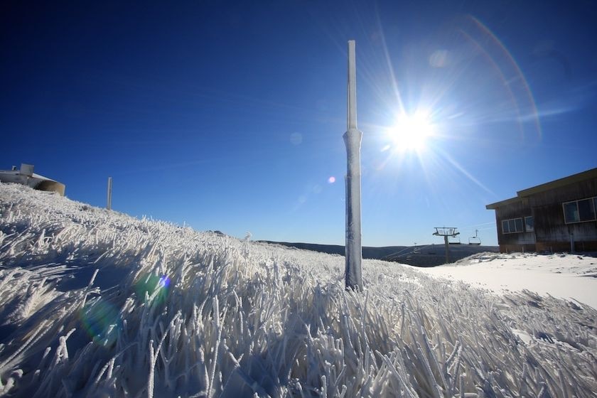 A photo of snow on the ground, with a blue sky and the sun in the background.