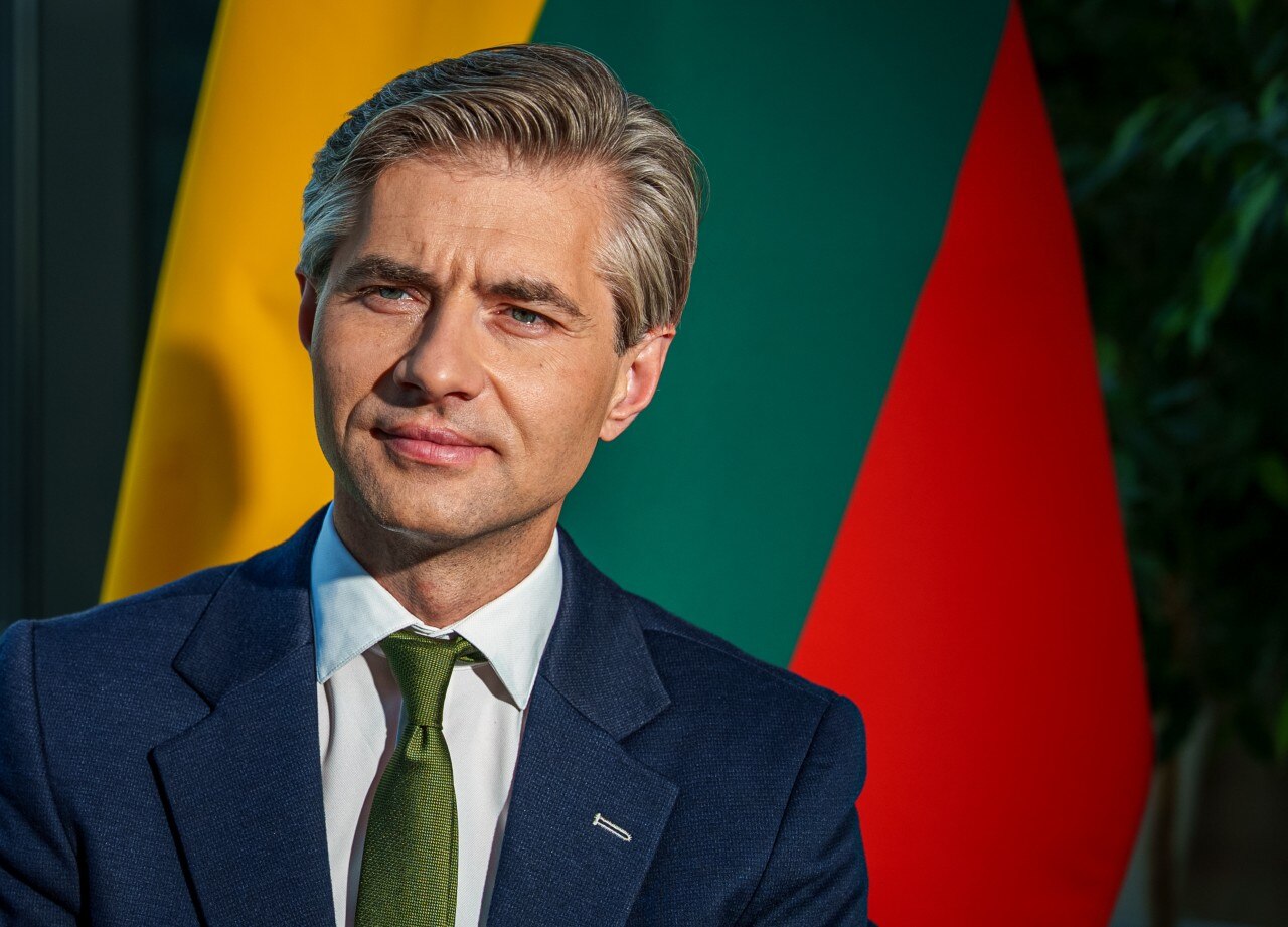 A man in a suit looking on, with a Lithuanian flag visible behind him.