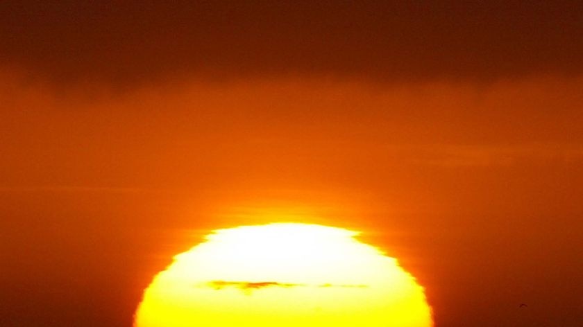 The outline of the sun shimmers in a heat haze at sunrise off the coast of Sydney.