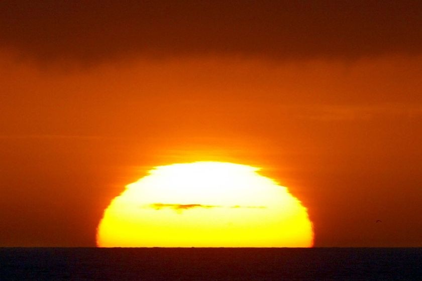 A large bright yellow sun sets on the red and orange horizon.
