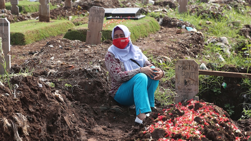 A woman in a hijab sits amongst graves in a cemetary. 