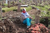 A woman in a hijab sits amongst graves in a cemetary. 