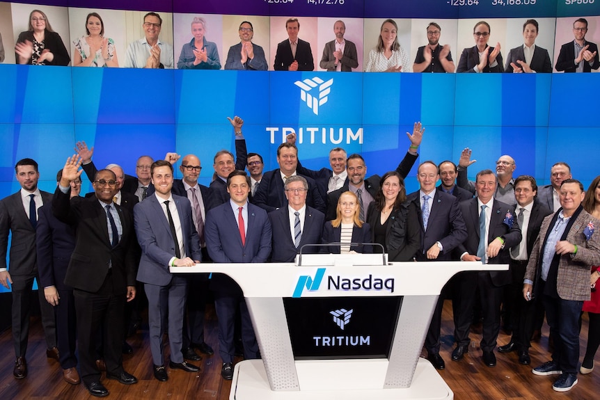 A few dozen employees in suits cheering with a Tritium logo in the background