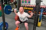 Jack Carroll lifts a barbell in a gym.