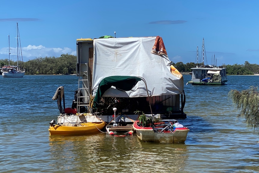 Tarpaulin-covered house boat with a fibreglass tender and kayak tied to rear of vessel.