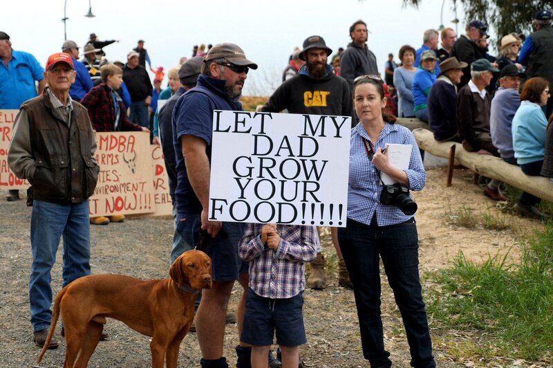 small child holds sign that says let my dad grow your food in front of face