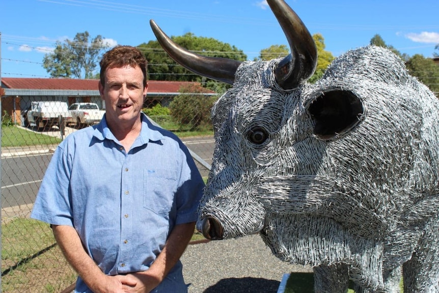 Man in blue shirt standing next to bull sculpture