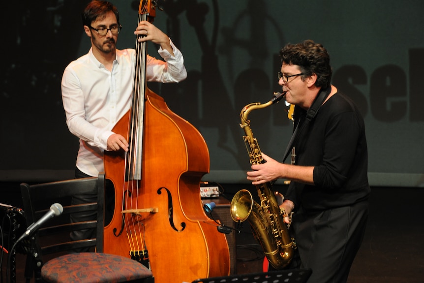Two men on stage with one playing the saxophone and one on a bass violin
