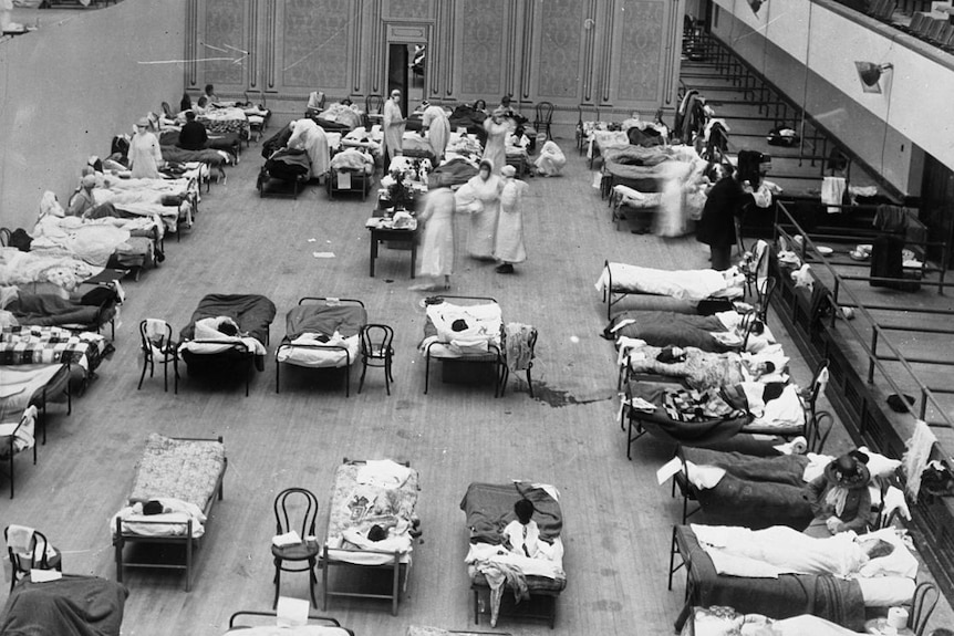 A black and white photo showing a view from above of a large room filled with nurses and people in hospital beds.