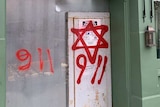 A green cafe shopfront shows a metal door sprayed with a red Star of David and two '9 11' phrases.