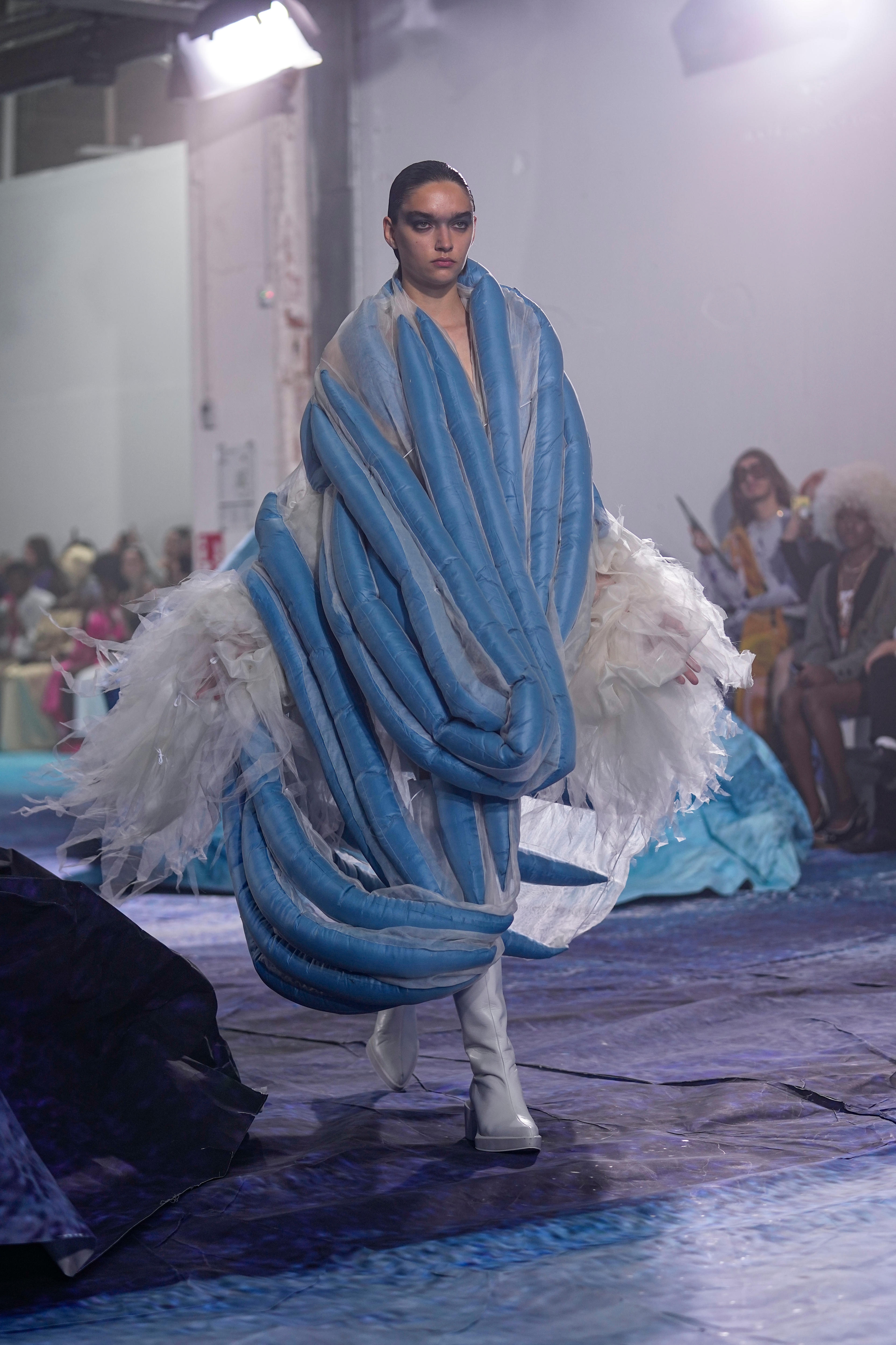 A model wears a blue garment with interesting shapes. 