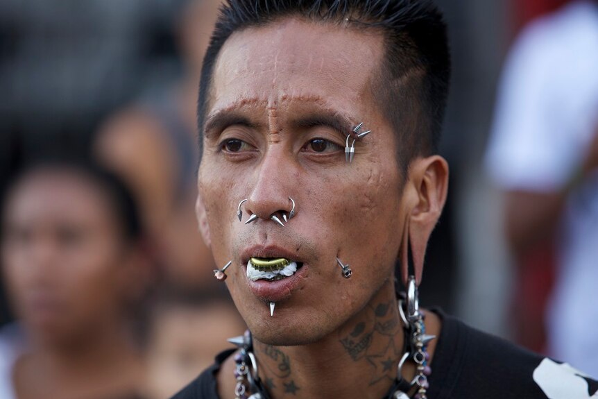 Man wears multiple piercings in eyebrows, nose, mouth, cheeks