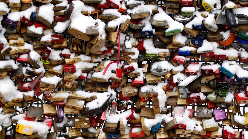 Snow covers padlocks attached to a fence at Cologne railway station.