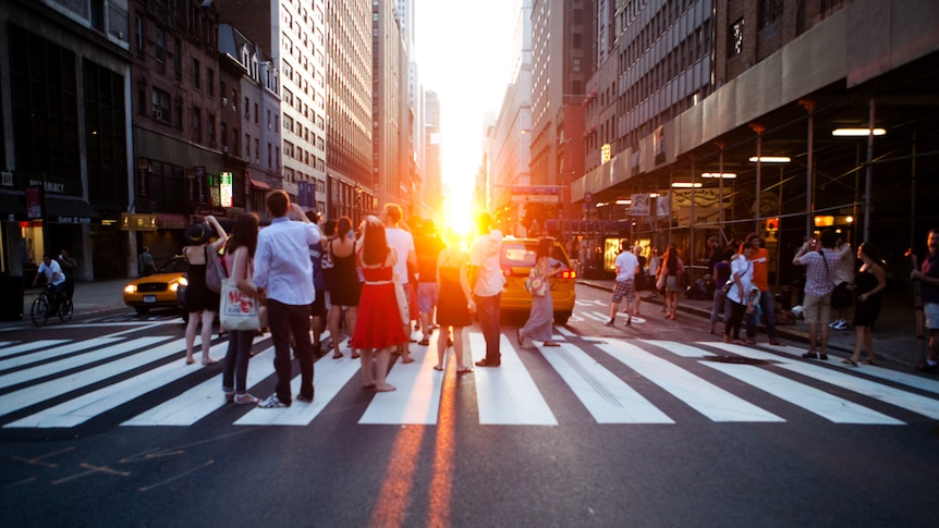 People stand on a pedestrian crossing to photograph a sunset.