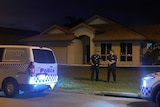 Two police officers standing between two police cars standing out the front of a house. 