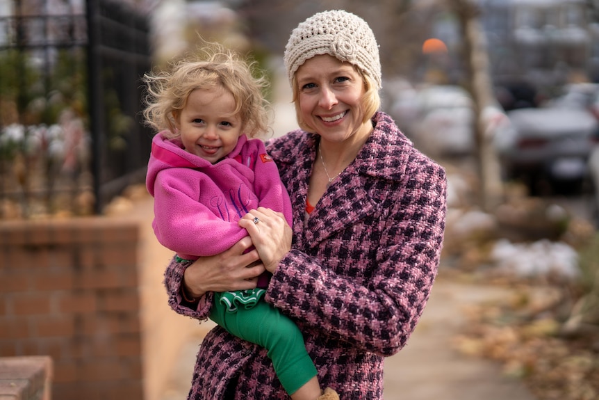 Woman holding her young daughter in her arms. Both are in pink jackets and coats.