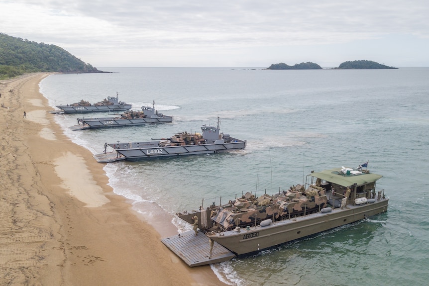 Aerial shot of army landing boats carrying battle tanks and troop carriers as they reach a sandy beach
