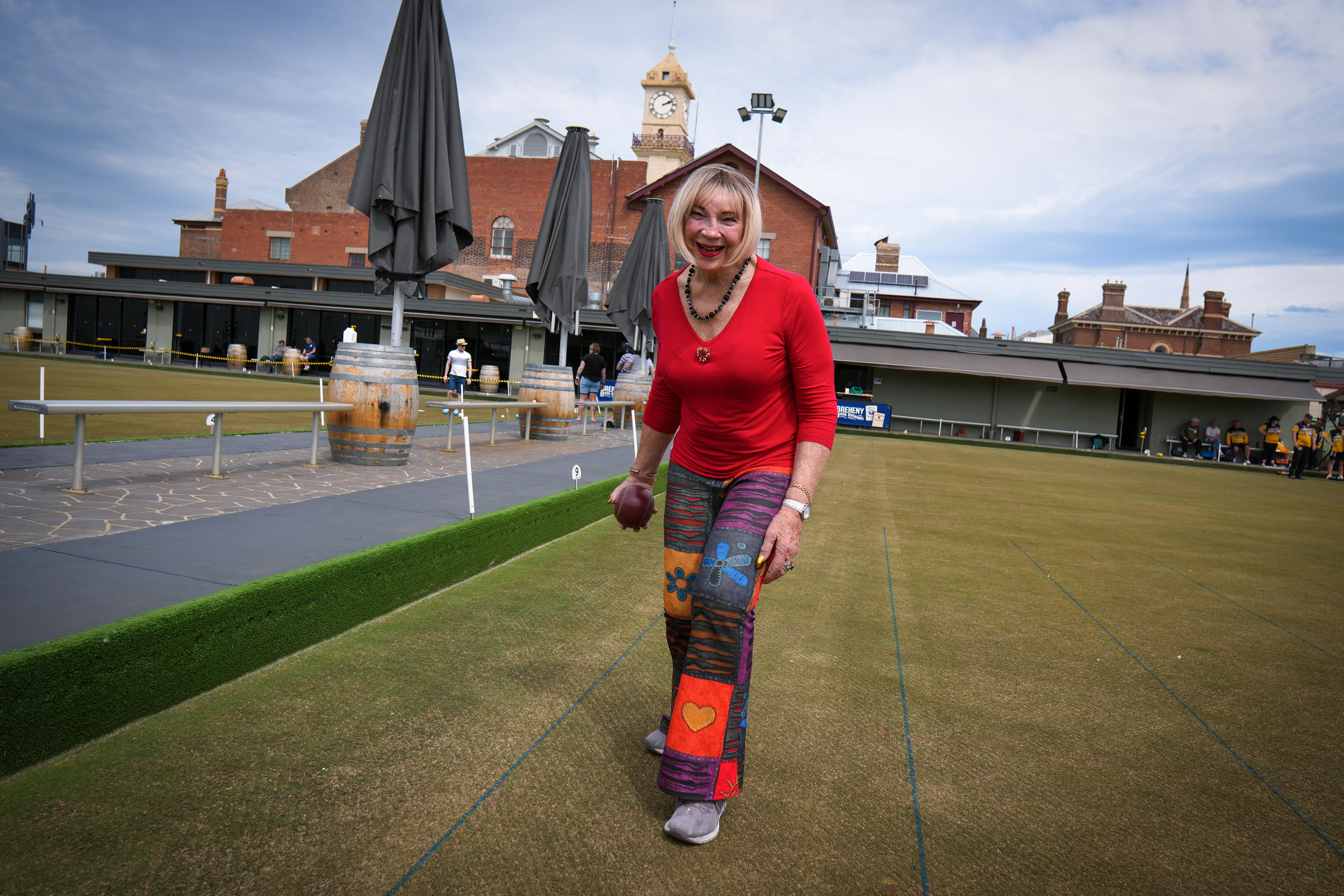 Uma mulher vestida com roupas coloridas se preparando para jogar boliche em um gramado verde.