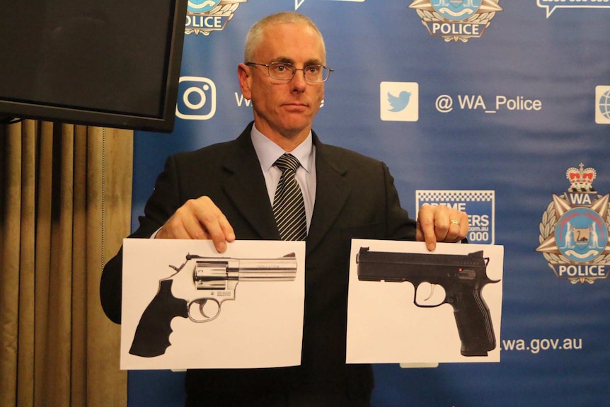 A man in a suit holds two pictures of handguns up to the camera.