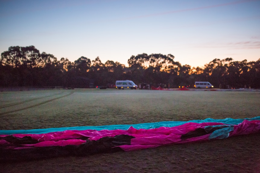A hot air balloon lies ready for inflation on frosty grass, with the lights of vans in the rear.