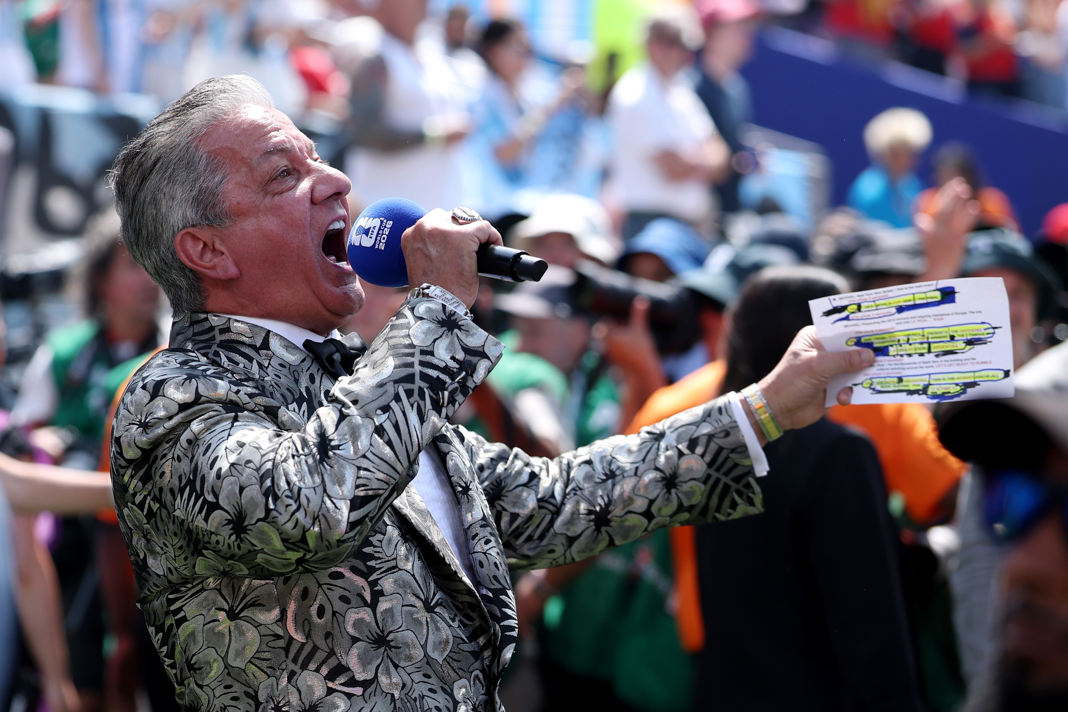 A man in a black-and-white, floral-patterned jacket bellows into a microphone.