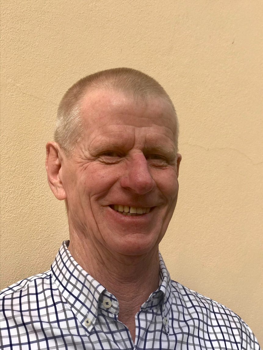 A smiling man with close-cropped hair, wearing a chequered shirt.