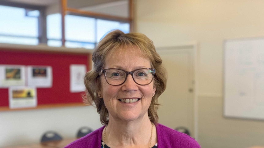 A middle aged woman with short light hair and glasses and smiling at the camera.