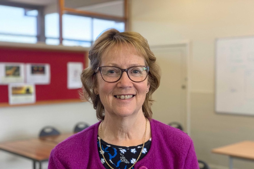 A middle-aged woman with short light hair and glasses and smiling at the camera.