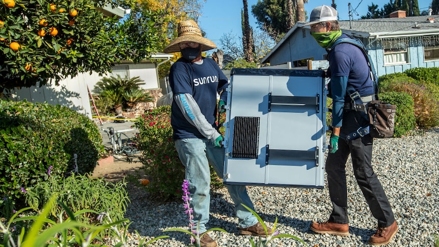 Two men carry a battery.