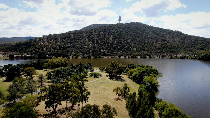 An aerial view of a lakeside park in the foreground, with a mountain topped by a tower in the background.