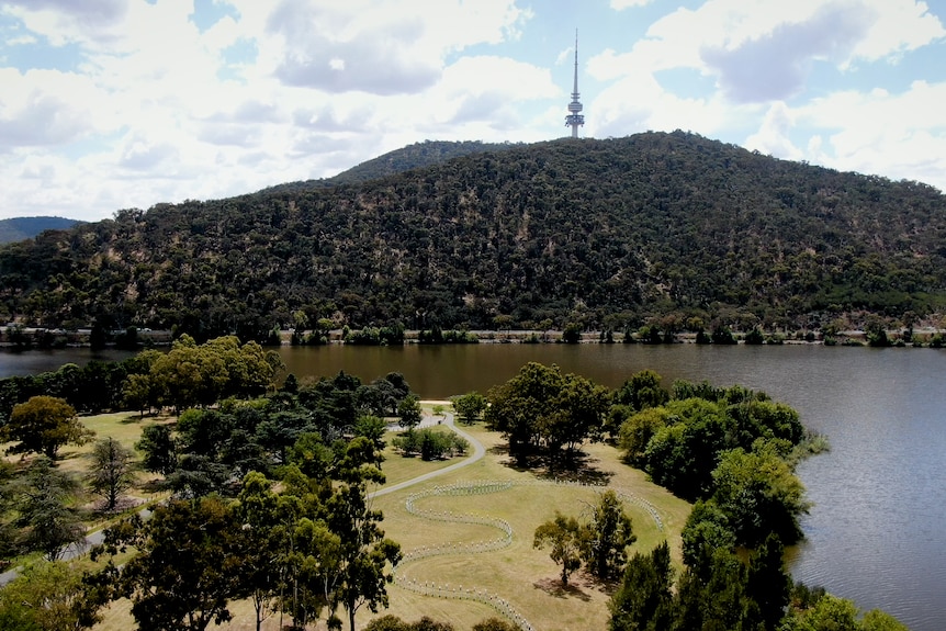An aerial view of a lakeside park in the foreground, with a mountain topped by a tower in the background.