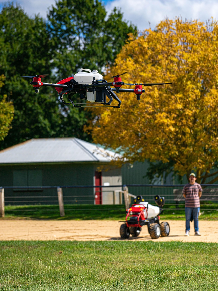 A drone in the air and an autonomous vehicle on the ground with a man standing beside it.