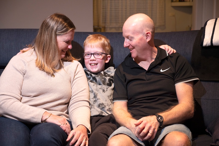 A smiling nine year old boy sitting on a sofa between his mum and dad, Ausnew Home Care, NDIS registered provider, My Aged Care