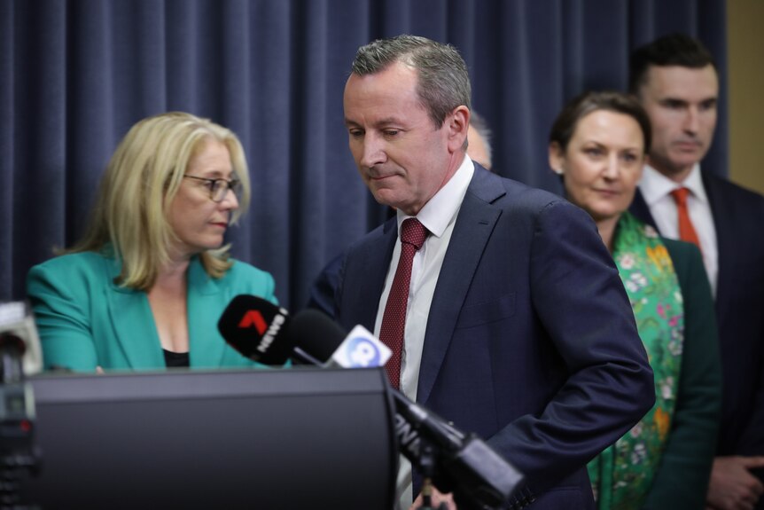 Mark McGowan steps to the podium at a media conference wearing a blue suit and red tie, with Labor colleagues behind him.