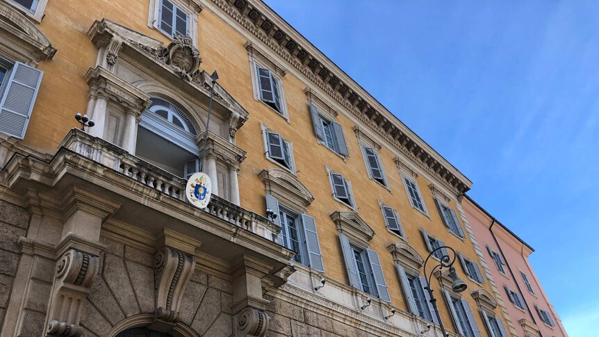 The outside of an ornate building in the Vatican, against a bright blue sky.