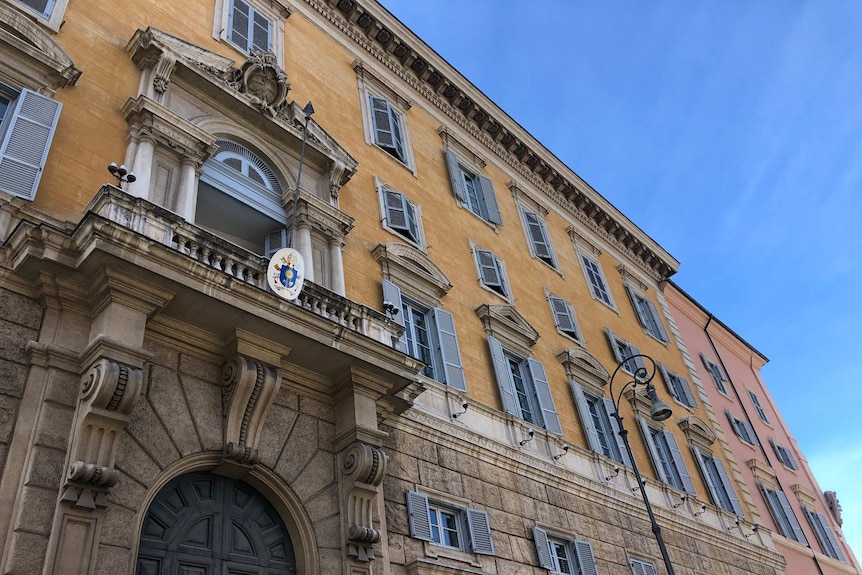 The outside of an ornate building in the Vatican, against a bright blue sky.