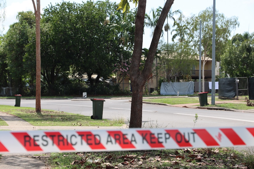 An intersection in a quiet suburb, with a strip of crime scene tape in the foreground. 