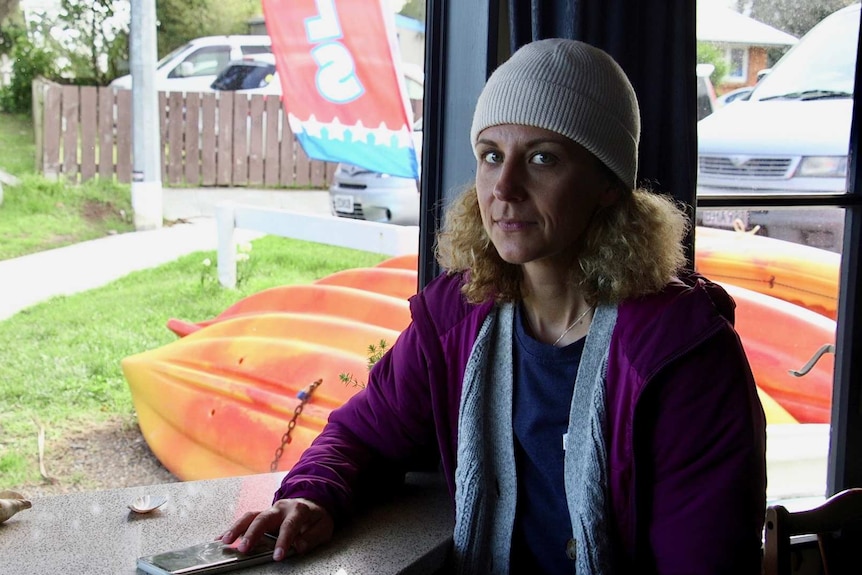 A woman with blonde hair wearing a beanie while sitting in front of a window.