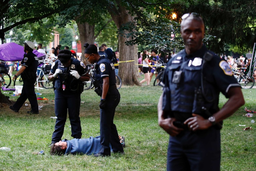 Woman lies on the ground in the park in a blanket while police stand nearby