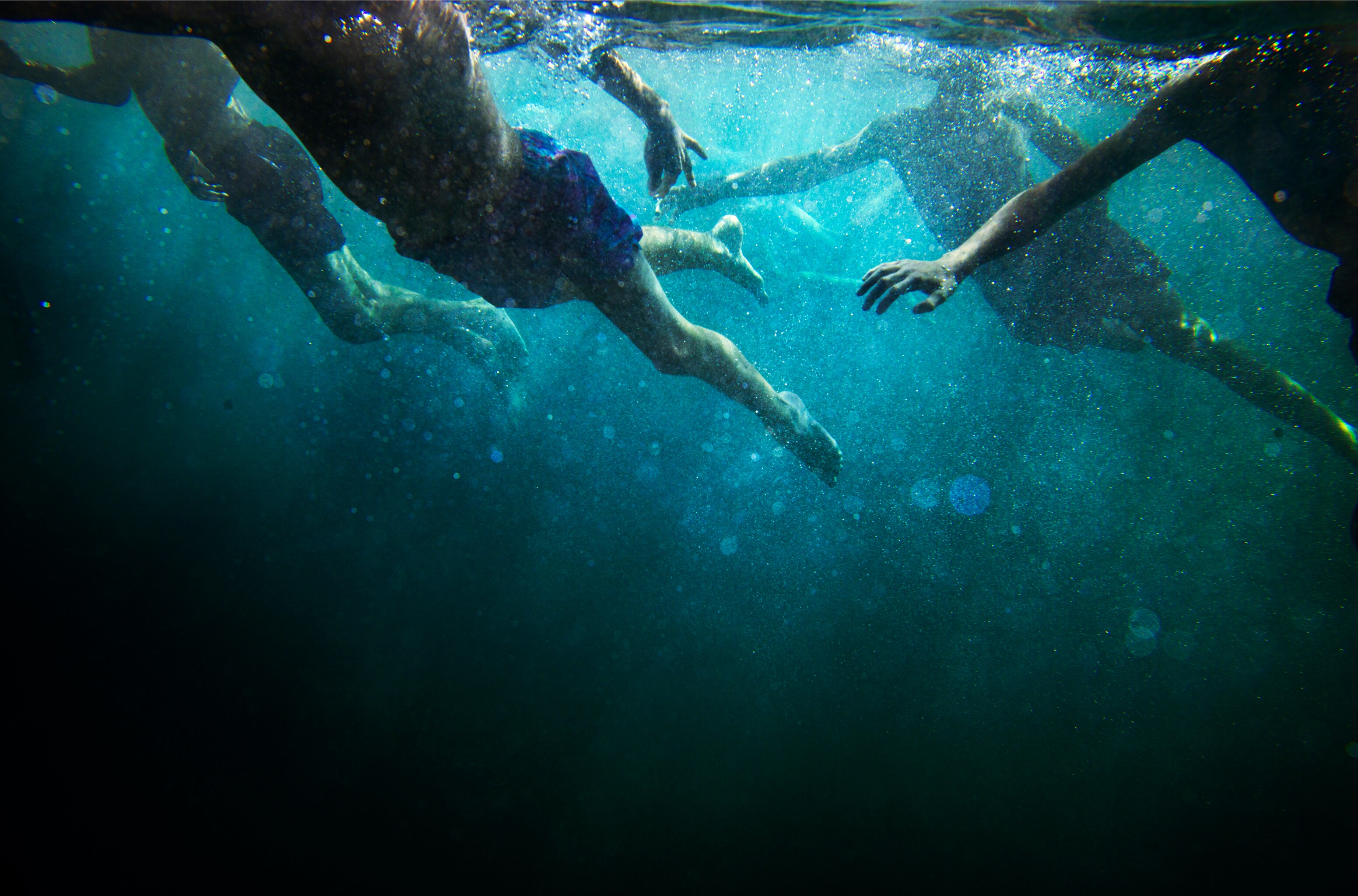 Image by Narelle Autio taken underwater, showing the figures of male swimmers moving through the water