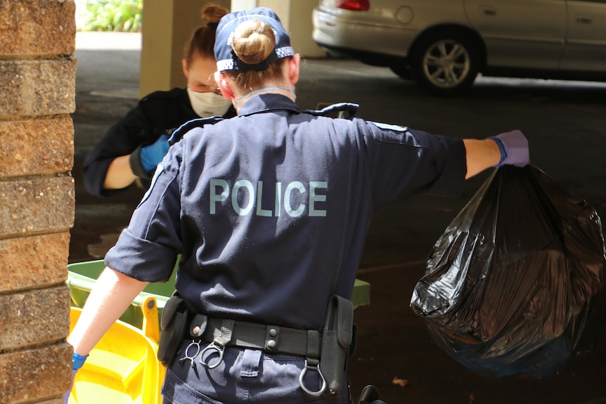Two police officers remove rubbish bags from garbage bins. 