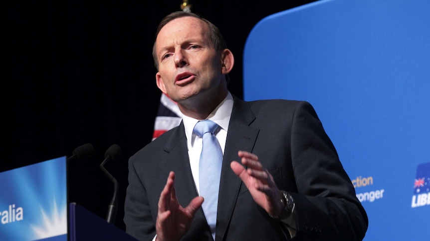 Former prime minister Tony Abbott stands at  a lecturn.