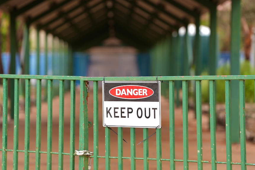 A 'danger: keep out' sign hands on a green fence at a school