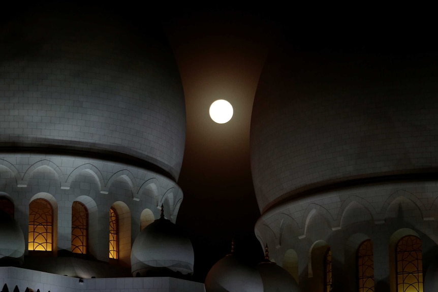 A lunar eclipse of a full "Blood Moon" rises behind the Sheikh Zayed Grand Mosque in Abu Dhabi.
