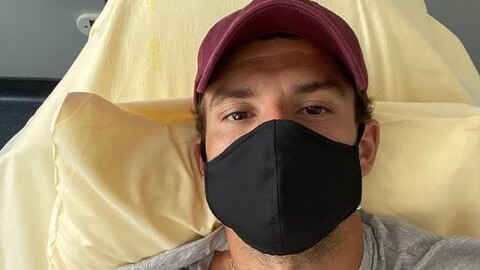 Tennis player Grigor Dimitrov wears a mask while lying in bed and flashing a peace sign.