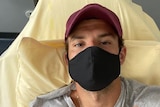 Tennis player Grigor Dimitrov wears a mask while lying in bed and flashing a peace sign.