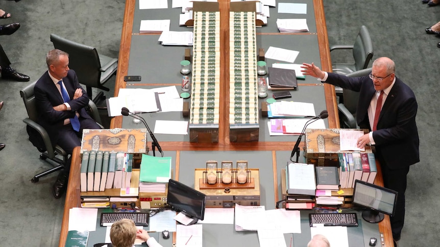 A man speaking in the parliament with his arm pointing across the chamber. Opposite him is a man sitting with his arms crossed.