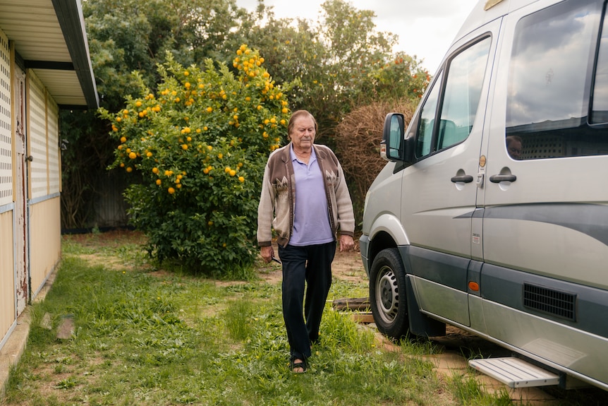 A man walks in a backyard near a silver campervan.